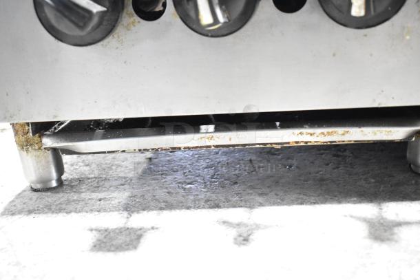 Commercial countertop gas charbroiler grill with visible control knobs and sturdy metal legs. Some rust and wear present.