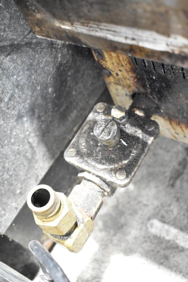 Rusty gas connection valve on commercial countertop gas-powered charbroiler grill, indicating well-used condition.