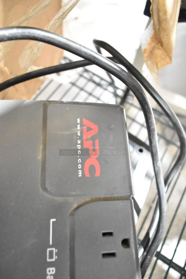 APC Uninterruptible Power Supply, black, visible logo, power cords attached, outlet shown, used condition.