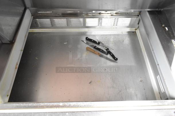 Beverage Air commercial prep table interior, showing stainless steel surface with scratches and three utility knives, indicating used condition.
