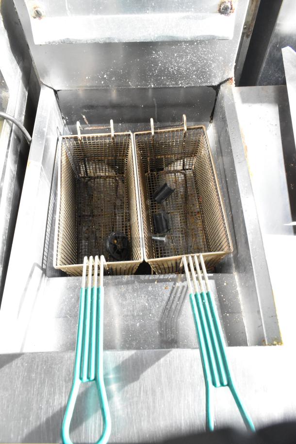 Frymaster commercial floor fryer with two metal fry baskets, used condition. Handles with green grips. Suitable for high-capacity frying.