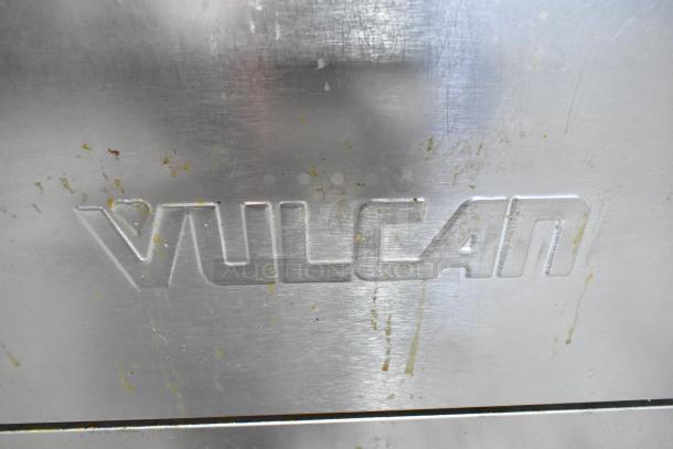 Vulcan commercial gas range logo on metal surface, showing minor scratches and stains, indicating use.