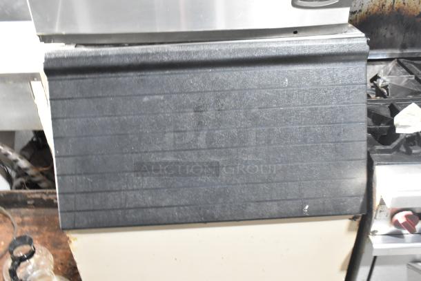 Manitowoc commercial ice machine head on ice bin, visible wear on black textured surface, stainless steel accents.