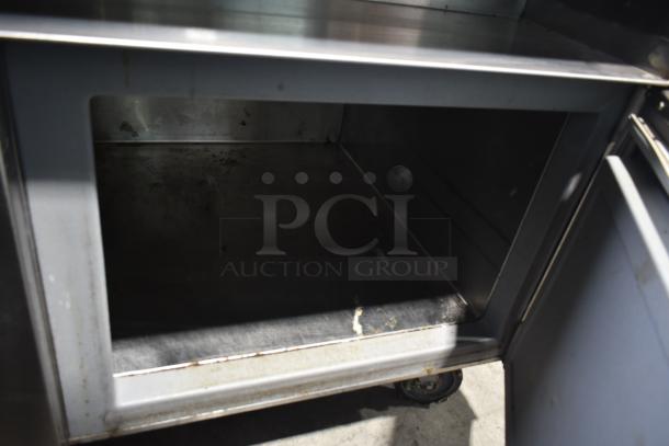 Commercial prep station with sturdy metal construction on commercial casters, showing interior storage, some wear visible.