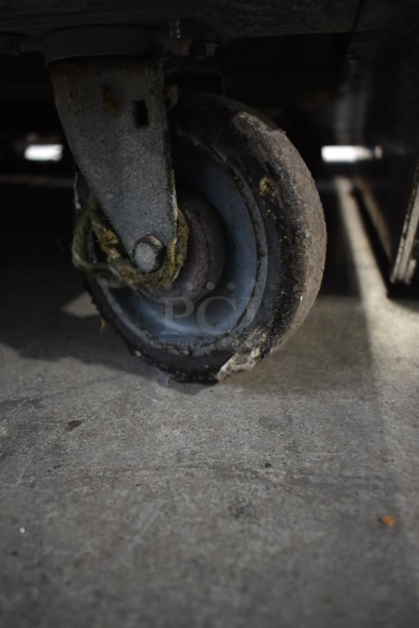 Commercial prep station caster wheel on concrete floor. Metal bracket and blue rubber wheel show signs of wear.