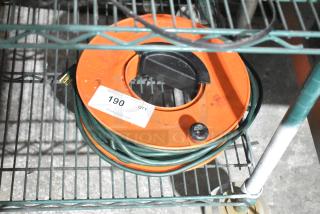 Orange extension cord reel with green cord, mounted on a metal shelf. Label reads "190 QTY" from PCI Auctions.