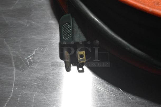Extension cord reel with black and green plug, slight wear, on a metallic surface.