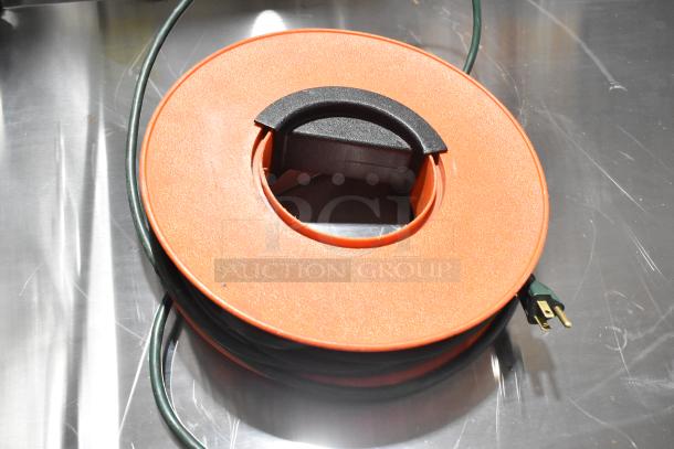 Orange extension cord reel with black handle, featuring a green cord and three-prong plug. Appears in good condition.