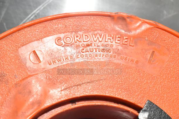 Orange Cordwheel Model 600 extension cord reel with caution marking to unwind before use. Visible wear, functional condition.