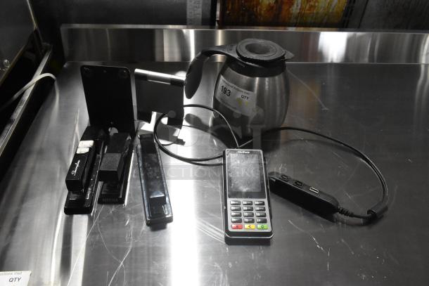 Seven-item lot including coffee pot, Verifone credit card reader, three staplers, phone holder, and a USB hub. Auction tag visible.