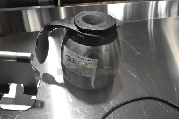 Stainless steel coffee pot with black handle, marked with auction label "193 QTY 7", on reflective surface.