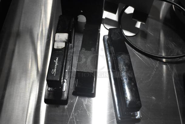 Three staplers on a metal surface, including Swingline and Bostitch brands; part of a lot with 7 various items.