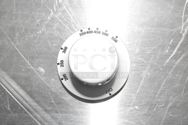 Close-up of a new oven knob on a metallic surface, marked with temperature settings from 200 to 550 degrees.
