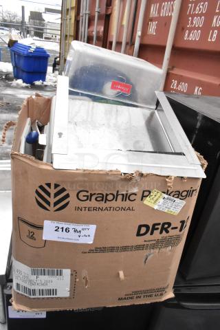 Lot of various items, including an Edlund knife holder and drop-in bins, in a worn cardboard box labeled "Graphic Packaging International."