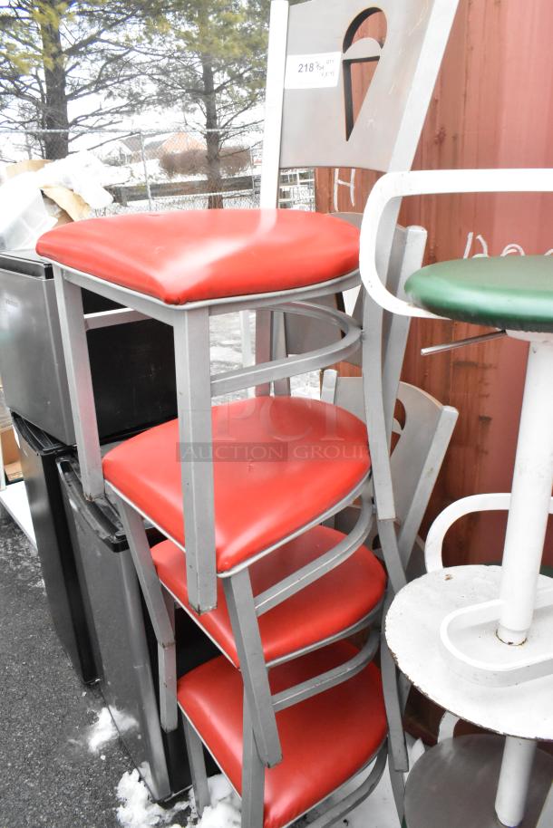 Stack of metal dining chairs with red seat cushions and a green stool. Rust and wear visible. Tag reads "218 QTY."
