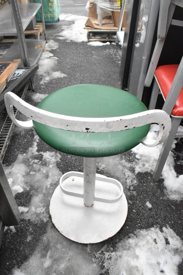 Metal dining height chair with a green seat cushion and white frame, slightly worn. Red seat chairs visible nearby.