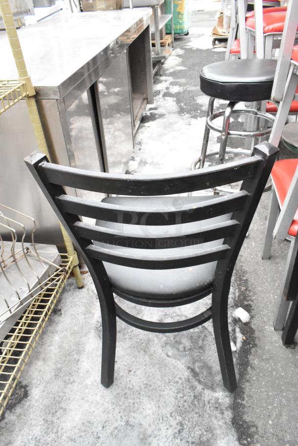 Metal dining chair with black frame and red seat cushion, back view. Includes part of a green stool in background.