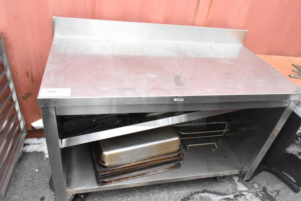 Commercial stainless steel table with backsplash and under shelf containing trays and racks, good condition.