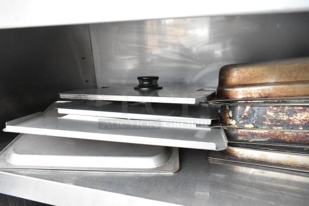 Commercial table with under shelf and back splash, containing multiple metal trays and sheets, moderate wear visible.
