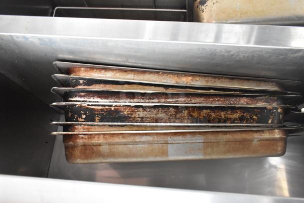 Commercial table with back splash and under shelf, includes worn pans. Visible corrosion on pans; sturdy stainless steel.