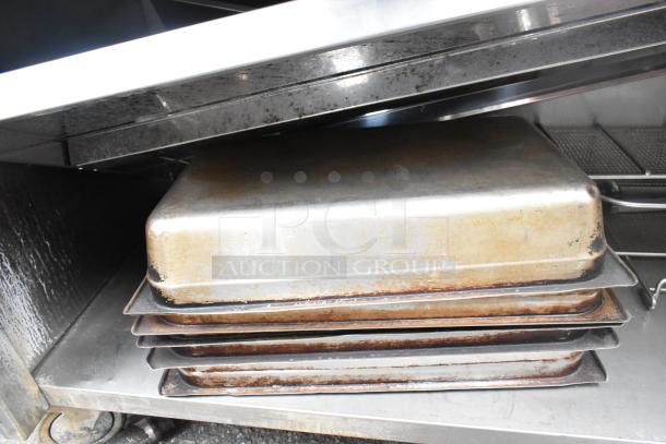 Commercial table with backsplash and under-shelf, includes baking trays. Stainless steel, used condition.