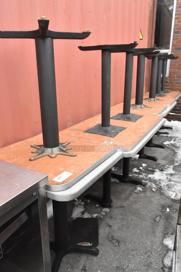 Set of 10 dining height tables with black metal bases, wood tops, labeled. Stacked outdoors, good condition.