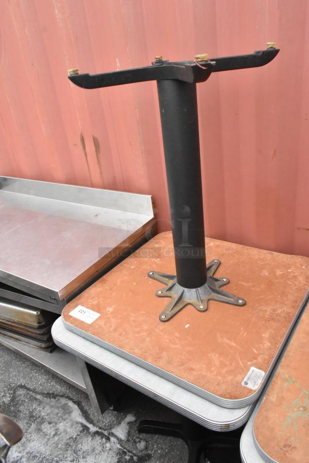 Dining height table on black metal base, shown upside down. Orange tabletop, slightly worn. Auction lot tag visible.