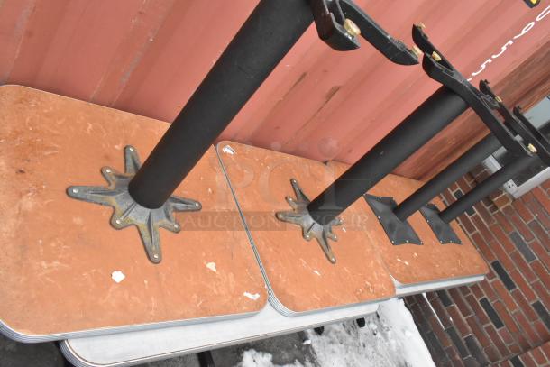 Stacked dining tables on sturdy black metal bases, showing minor wear. Set of 10, ideal for commercial use.