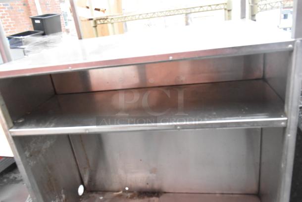 Stainless steel shelving unit with two shelves, visibly worn with rust and marks, suitable for industrial storage.