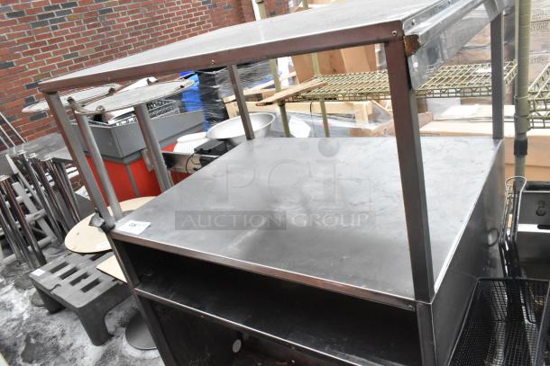 Metal shelving unit with two tiers, sturdy construction. Visible surface wear, indicative of prior use. Square design.