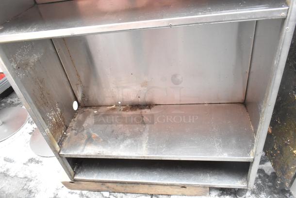 Metal shelving unit with two shelves, visible wear and rust spots. Industrial design, suitable for storage use.