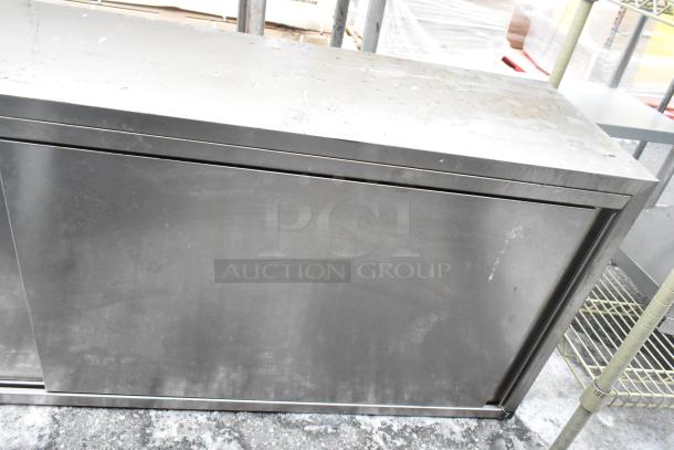 Steel two-door cabinet with a brushed finish, showing signs of wear. Rectangular shape, no visible brand or markings.