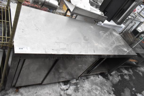 Stainless steel counter with two doors, under shelf, and signs of wear. Auction label "232" visible.