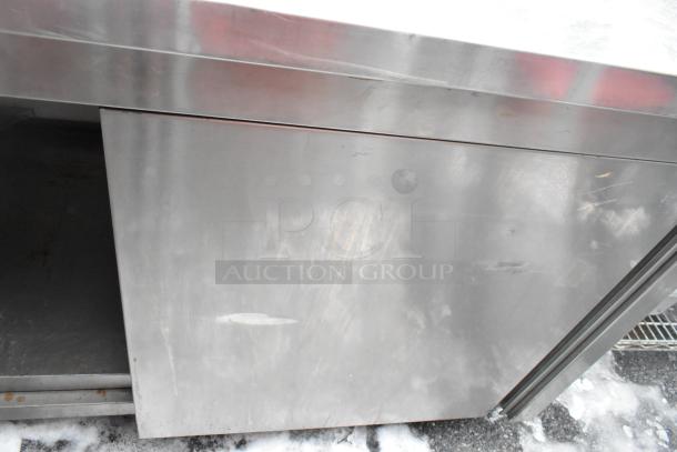 Stainless steel counter with two doors and an undershelf. Shows surface scuffs and slight discoloration, indicating used condition.