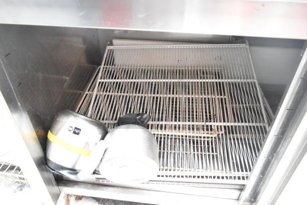 Stainless steel counter with two doors and under shelf, used condition, visible wire shelf; pots included underneath.