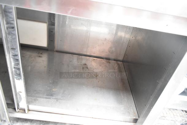 Stainless steel counter with two doors, under shelf. Slight surface wear visible, ideal for kitchen storage.