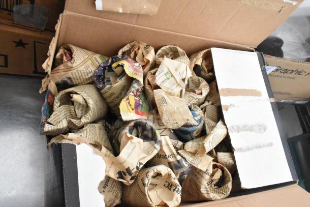 Cardboard box containing glasses and bowls wrapped in newspaper, part of Regency 600TSB3036S table contents.
