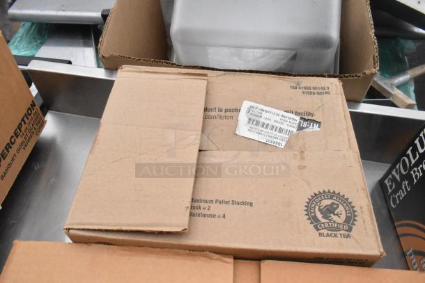 Cardboard boxes labeled "Rainforest Alliance Certified Black Tea" and "Evolution Craft Brewing Co." atop a metal table.