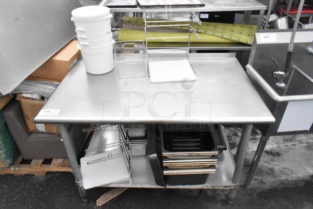 Commercial stainless steel table with under shelf and contents. Includes storage bins, metal rack, and containers. Good condition.