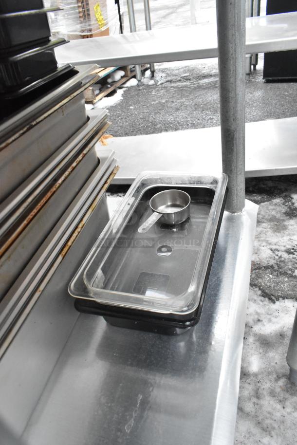 Commercial table with under shelf, includes metal pans and containers, in used condition, outdoor setting.