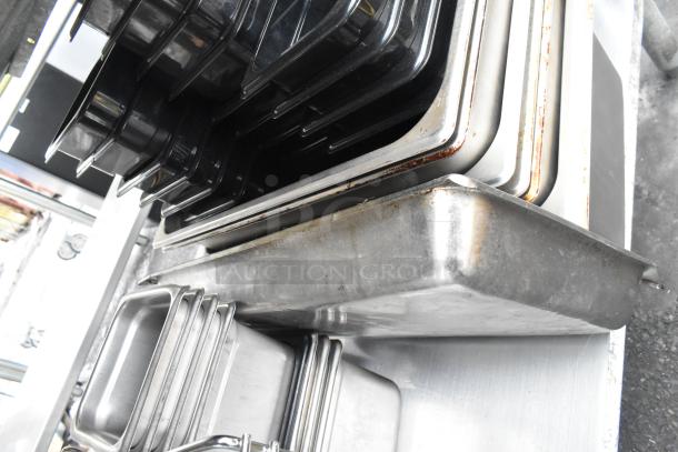 Commercial table with under shelf, containing various metal and plastic trays; used condition, some rust visible.