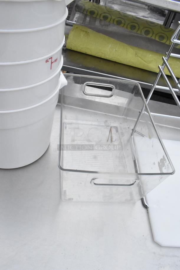 Commercial table with under shelf, featuring clear storage bins and stacked white containers. Good condition.