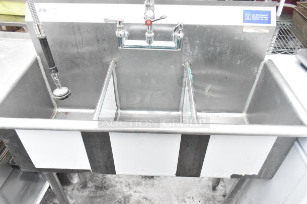 Commercial 3 bay sink with faucet, handles, and spray nozzle. Stainless steel, moderate wear, L&E label visible.