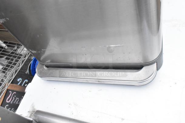 Chrome trash can with minor scratches, pedal-operated; part of a 2-piece lot with a black poly trash can, auction item.