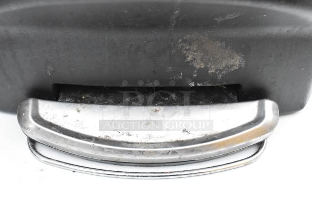 Black poly trash can with chrome foot pedal, showing wear and dirt accumulation.