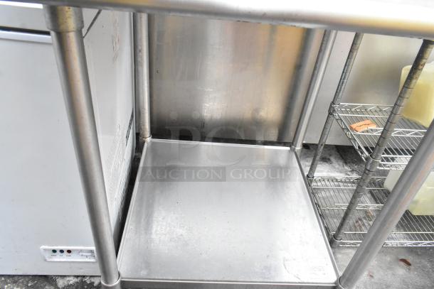 Stainless steel table with backsplash, under shelf; sturdy, used condition; ideal for kitchens or industrial settings.
