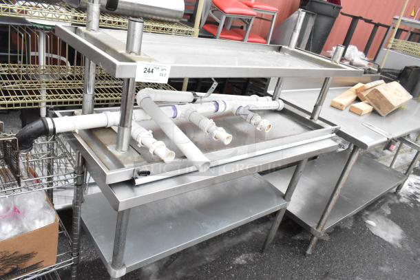 Two stainless steel tables with under shelves, visible wear, includes plumbing attachments, auction label "244," bid doubled.