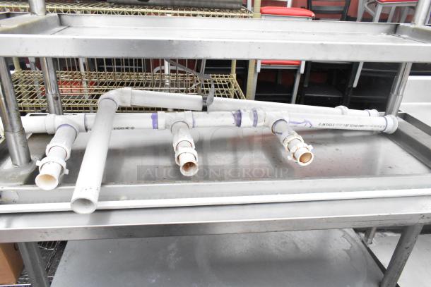 Two stainless steel tables with under shelf; visible plumbing components on tabletop; good condition.