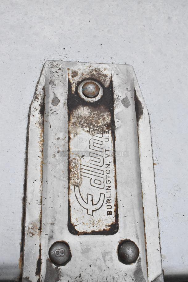 Commercial table with Edlund can opener mount, backsplash, and under shelf. Features signs of wear and rust, marked "Edlund, Burlington VT, U.S.A."