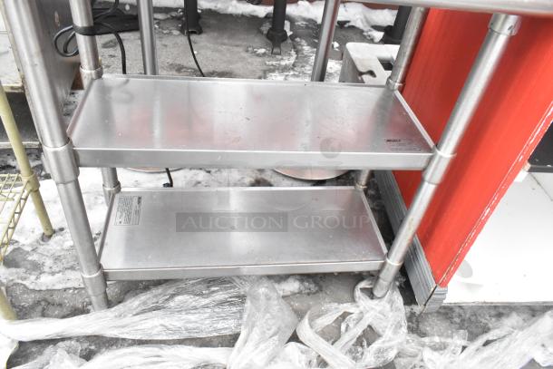 Commercial table with backsplash and two under shelves, stainless steel, used condition, visible manufacturer label.